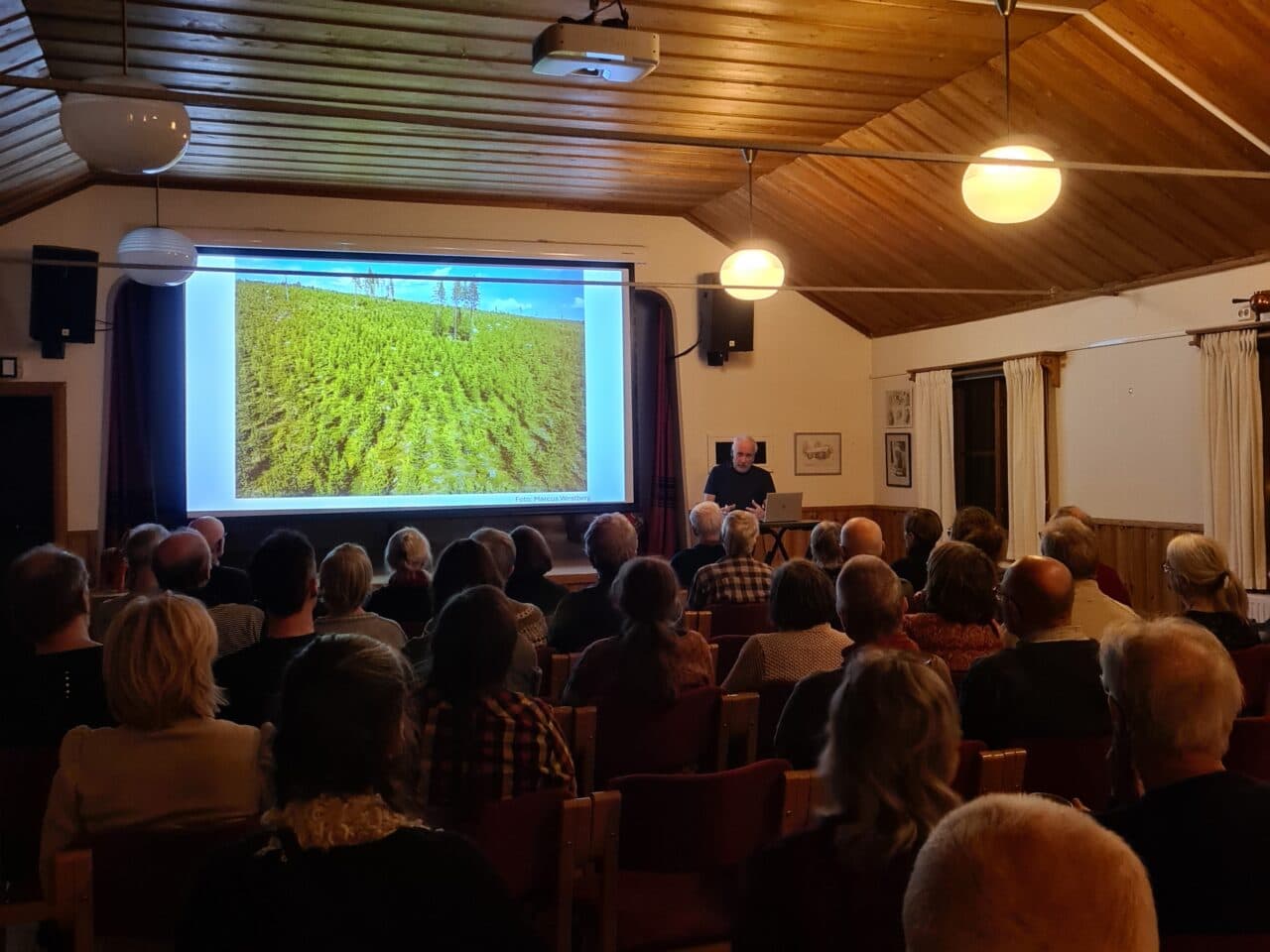 Föreläsningens publik bakifrån och på duken en bild från föreläsarens presentation.